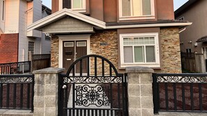 A two-story house with a stone facade, a brown roof, and a black gate with intricate designs. - Spacious upper-level unit located on Main St. (Vancouver)