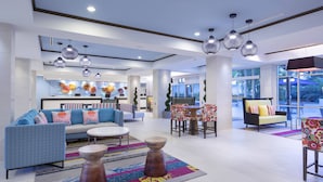Un hall d’hôtel moderne avec un canapé, des fauteuils, un coin repas et un comptoir d’accueil.