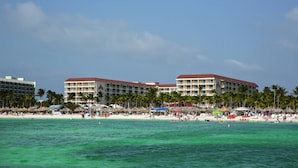 A beachfront hotel with multiple balconies, palm trees, and beach umbrellas.