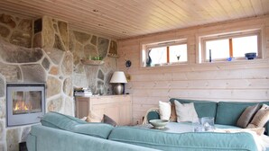 A cozy room with a stone fireplace, wooden walls, a teal sofa, and a window with shelves above. - Cozy home in Norheimsund with sauna (Norheimsund)