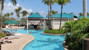 Un espace piscine avec des chaises longues, un bar couvert et des palmiers.