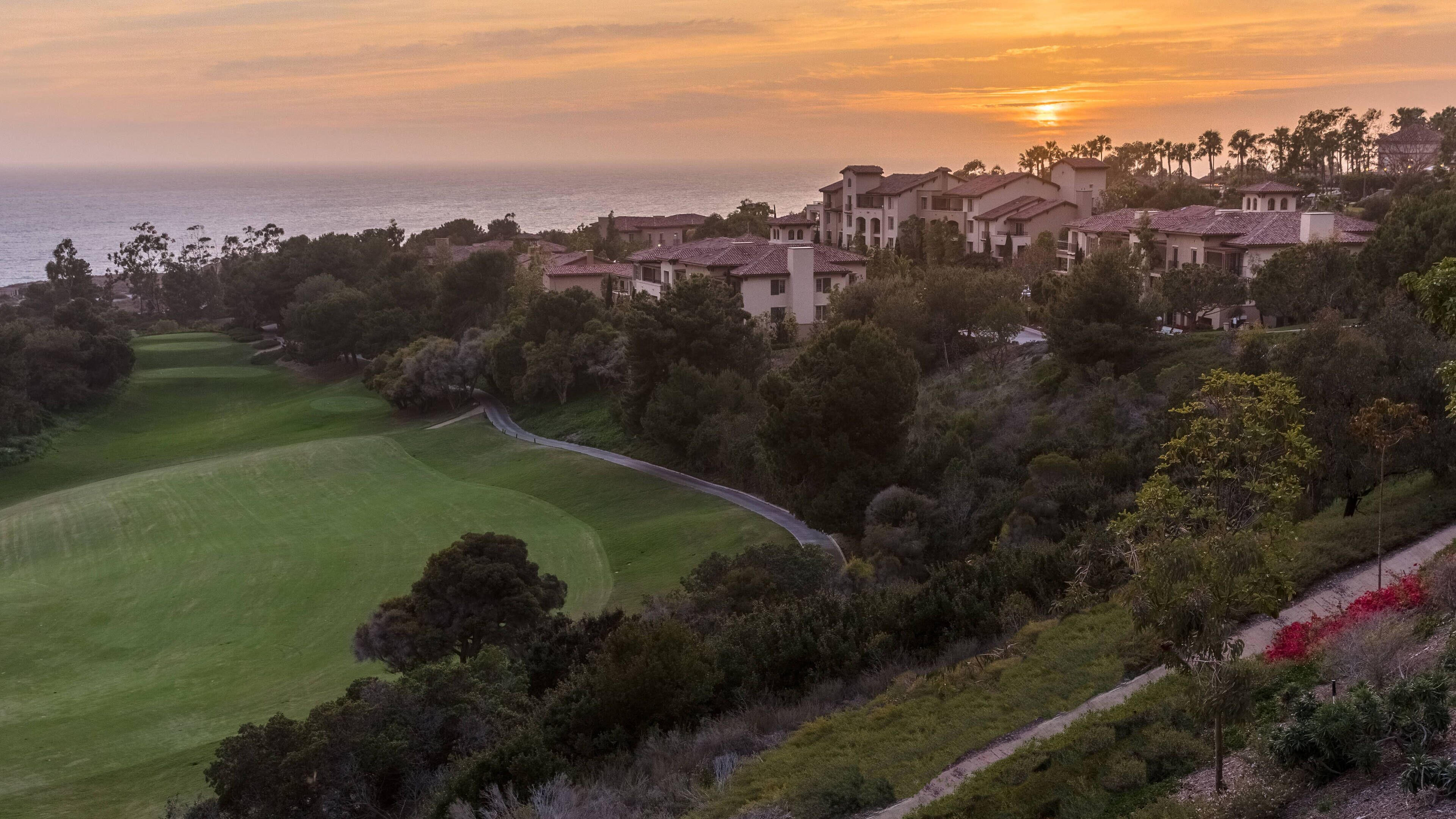 A golf course with a view of a coastal area and residential buildings in the background.