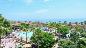 Een resort met een groot zwembad, omringd door palmbomen en ligbedden, met uitzicht op de kust.