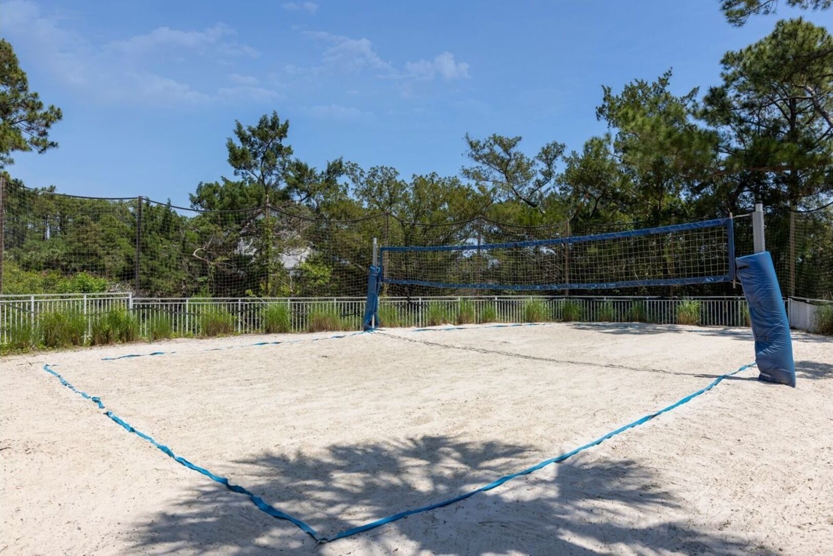 An outdoor volleyball court with a net, surrounded by a fence and trees.