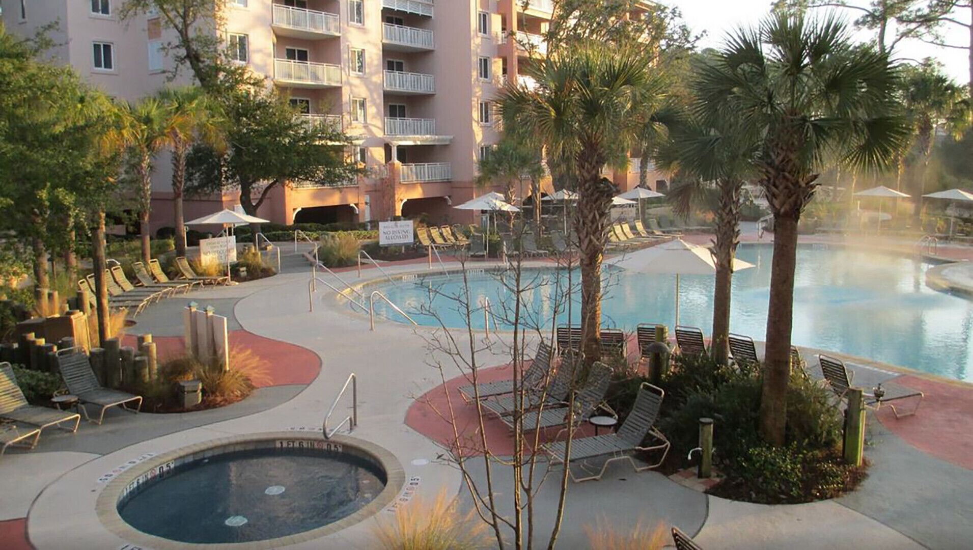 Un espace piscine avec des chaises longues, un jacuzzi et un bâtiment doté de balcons.