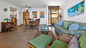 A spacious living area with a dining table, comfortable seating, and a view of the beach through an open door. - Oceanfront Maui Escape with Private Lanai, Pool & Stunning Views (Lahaina)