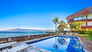 A swimming pool with lounge chairs, a view of the ocean, and a building with a sloped roof. - Oceanfront Maui Escape with Private Lanai, Pool & Stunning Views (Lahaina)
