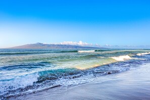 Ein Strand mit Wellen, blauem Himmel und fernen Bergen.