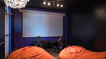Una habitación con pantalla de proyector, dos sillones de peluche, un sillón de gaming y una lámpara en el techo.
