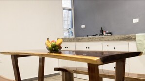 Une cuisine avec une table et un banc en bois, un panier de fruits sur la table et une fenêtre donnant sur des arbres.