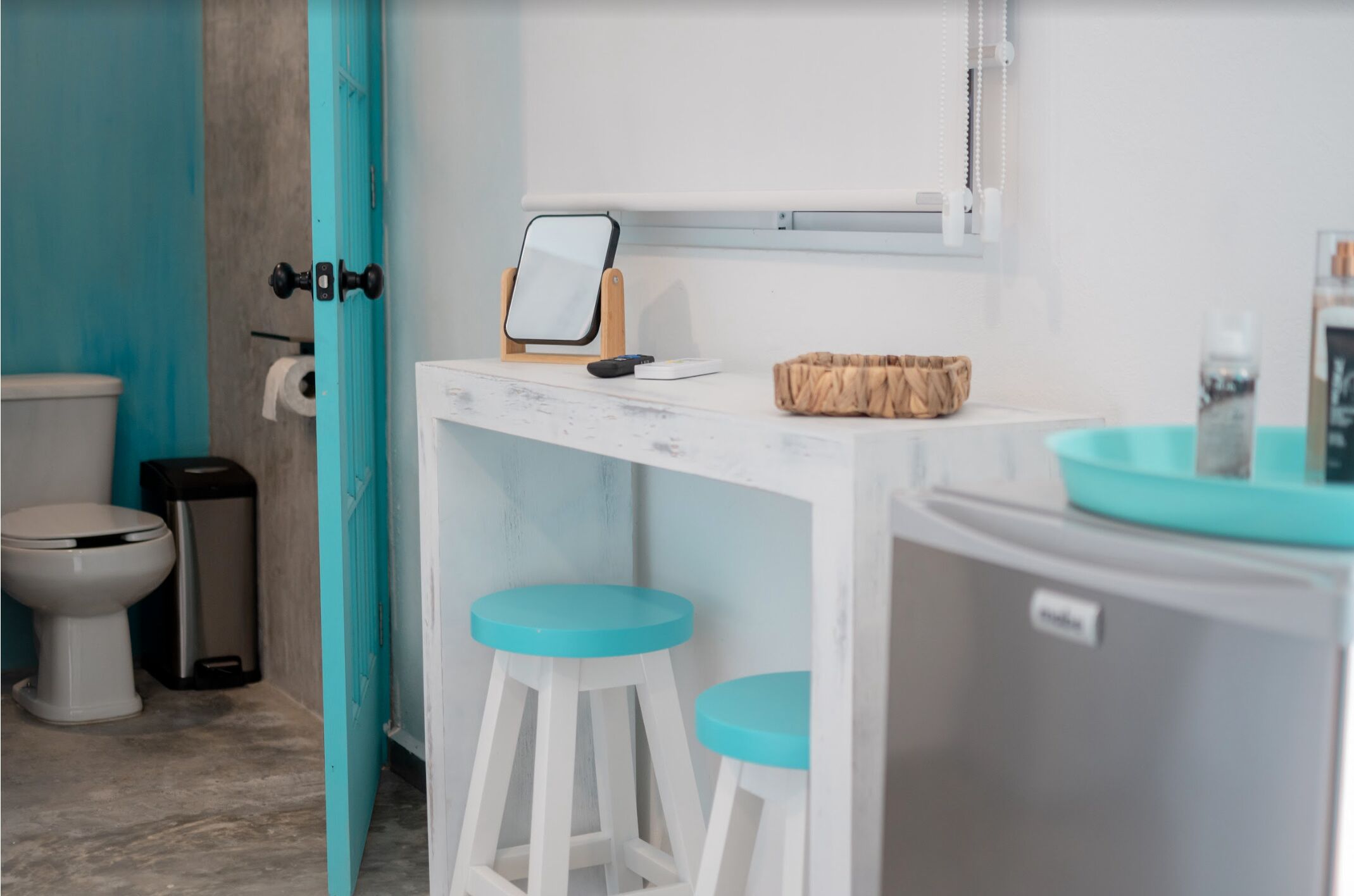 Un baño con inodoro, bidé, cubo de basura, un tocador blanco con espejo y dos taburetes azules.