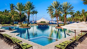 A pool area with multiple pools, palm trees, lounge chairs, and umbrellas.