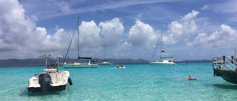 A marina with several boats anchored in clear turquoise water, surrounded by mountains in the background.