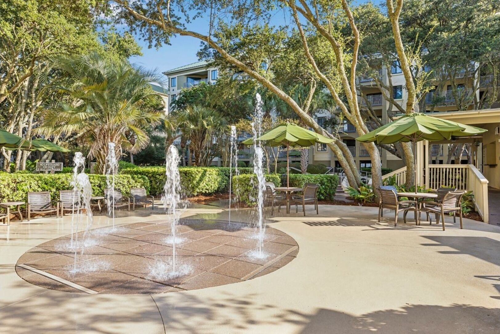 A courtyard with a central water feature, outdoor seating, and surrounding trees.