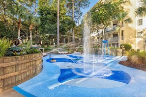 Una fontana con elementi decorativi in mosaico blu, immersa nel verde e delimitata da una recinzione in legno.
