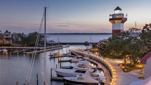 A marina with boats docked, a lighthouse, and a building with outdoor seating.
