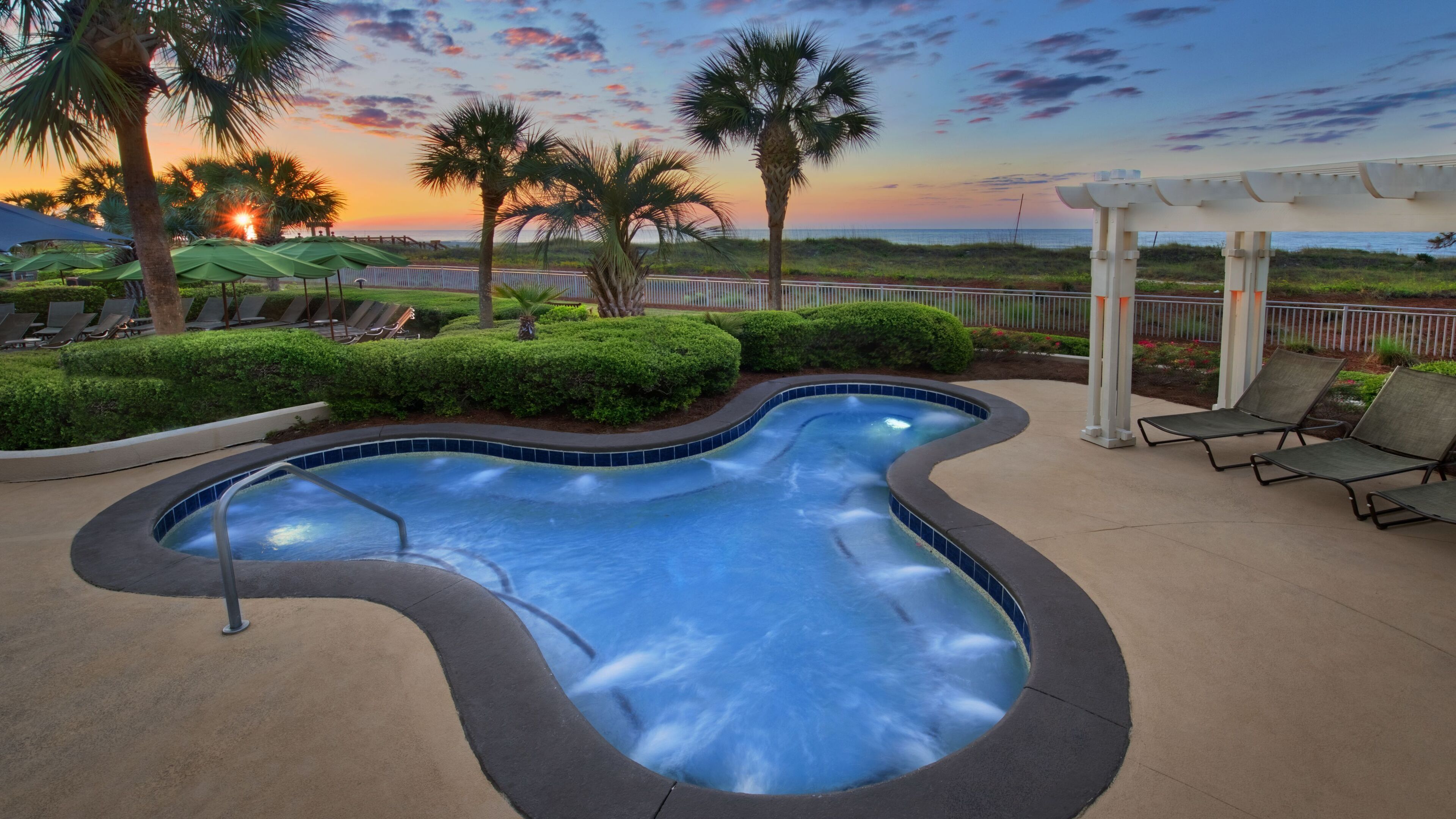 A swimming pool with a curved edge, surrounded by lounge chairs and palm trees.