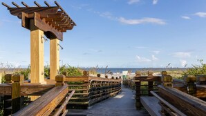 A wooden boardwalk leading to a beach with a wooden pergola structure.