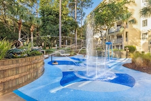 Un élément décoratif aquatique comprenant une fontaine et un motif en mosaïque bleue, situé dans une cour entourée d’arbres et d’un bâtiment.