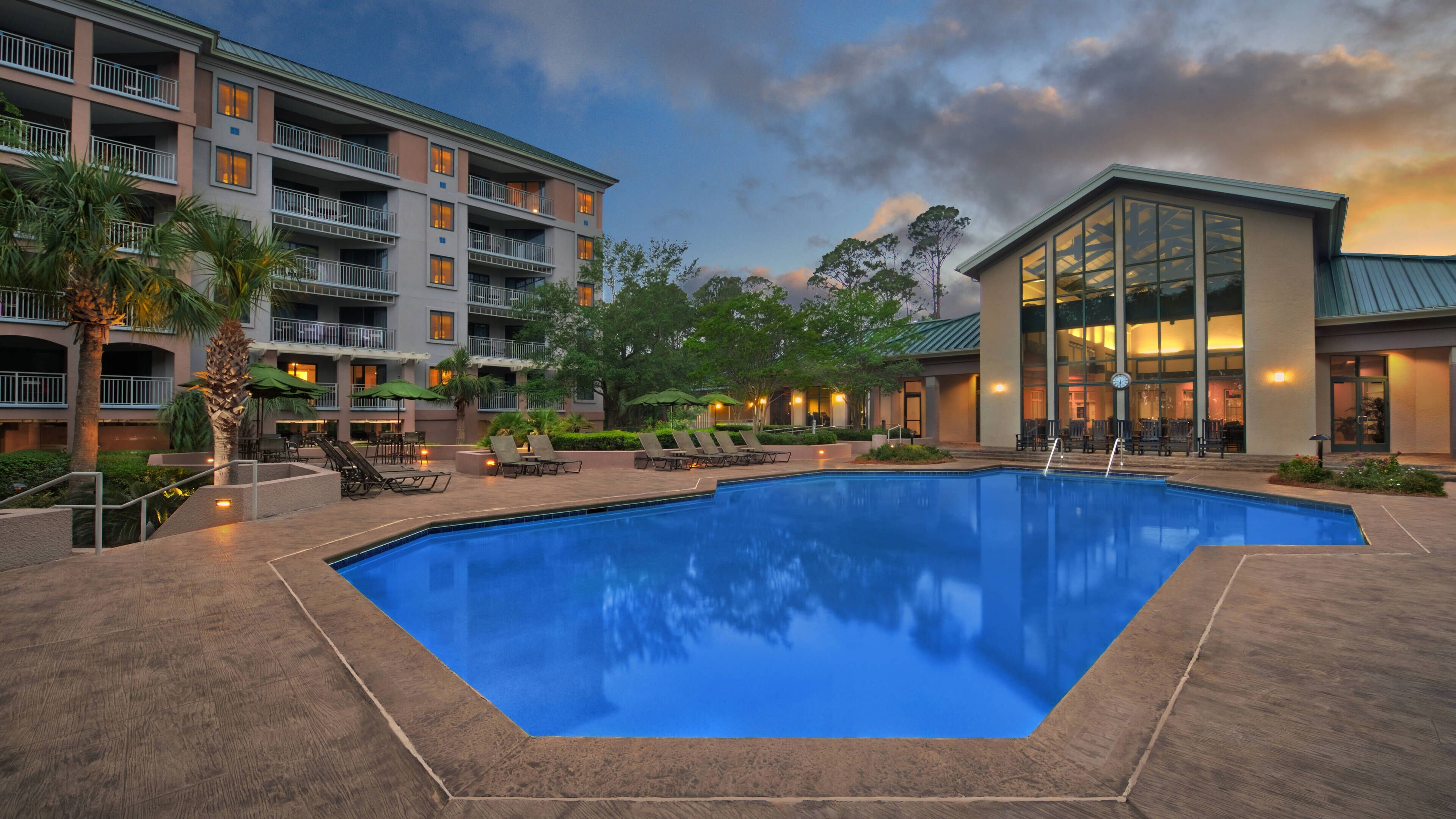 A hotel with a swimming pool, outdoor seating, and a building with multiple balconies.