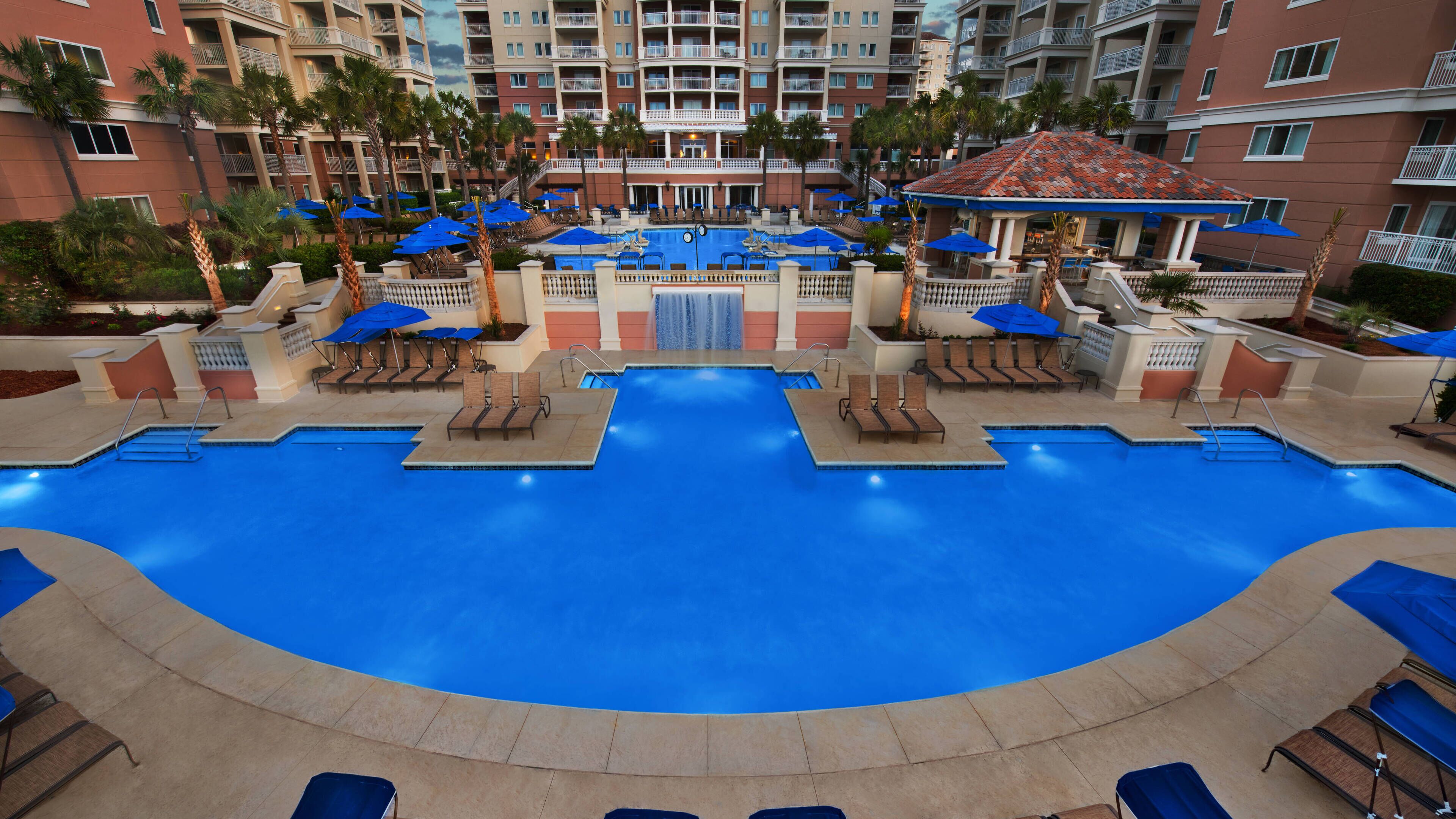 A large indoor swimming pool with multiple lanes, surrounded by lounge chairs and umbrellas.