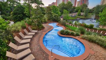A landscaped pool area with a winding water feature, surrounded by lush greenery and a series of lounge chairs.