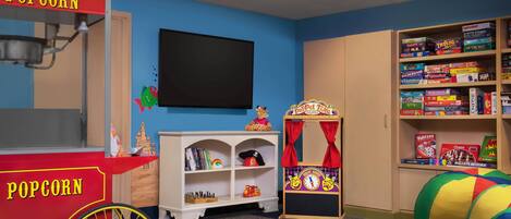 Een kinderspeelkamer met een popcornwagen, een boekenkast vol gezelschapsspellen en een poppenkast.