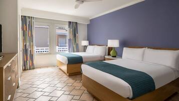Een hotelkamer met twee bedden, een plafondventilator, een raam met gordijnen en een televisie op een dressoir.