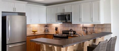 Cocina moderna con armarios blancos, electrodomésticos de acero inoxidable, una isla central con taburetes y un colgador de cuchillos.