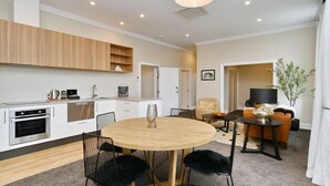 A modern kitchen with white cabinets, a built-in oven, and a dining area with a round table and chairs. - Kaiapoi Luxury Accommodation 1 -Historic and Luxury Apartment in Kaiapoi (Kaiapoi)