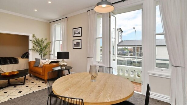 A modern living room with a round wooden table, a sofa, and a large window with curtains. - Kaiapoi Luxury Accommodation 1 -Historic and Luxury Apartment in Kaiapoi (Kaiapoi)