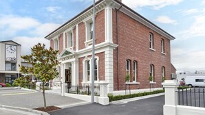 A two-story brick building with a central entrance, large windows, and a clock on the left. - Kaiapoi Luxury Accommodation 1 -Historic and Luxury Apartment in Kaiapoi (Kaiapoi)