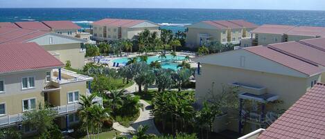 A resort with multiple buildings, a central swimming pool, and a view of the ocean.