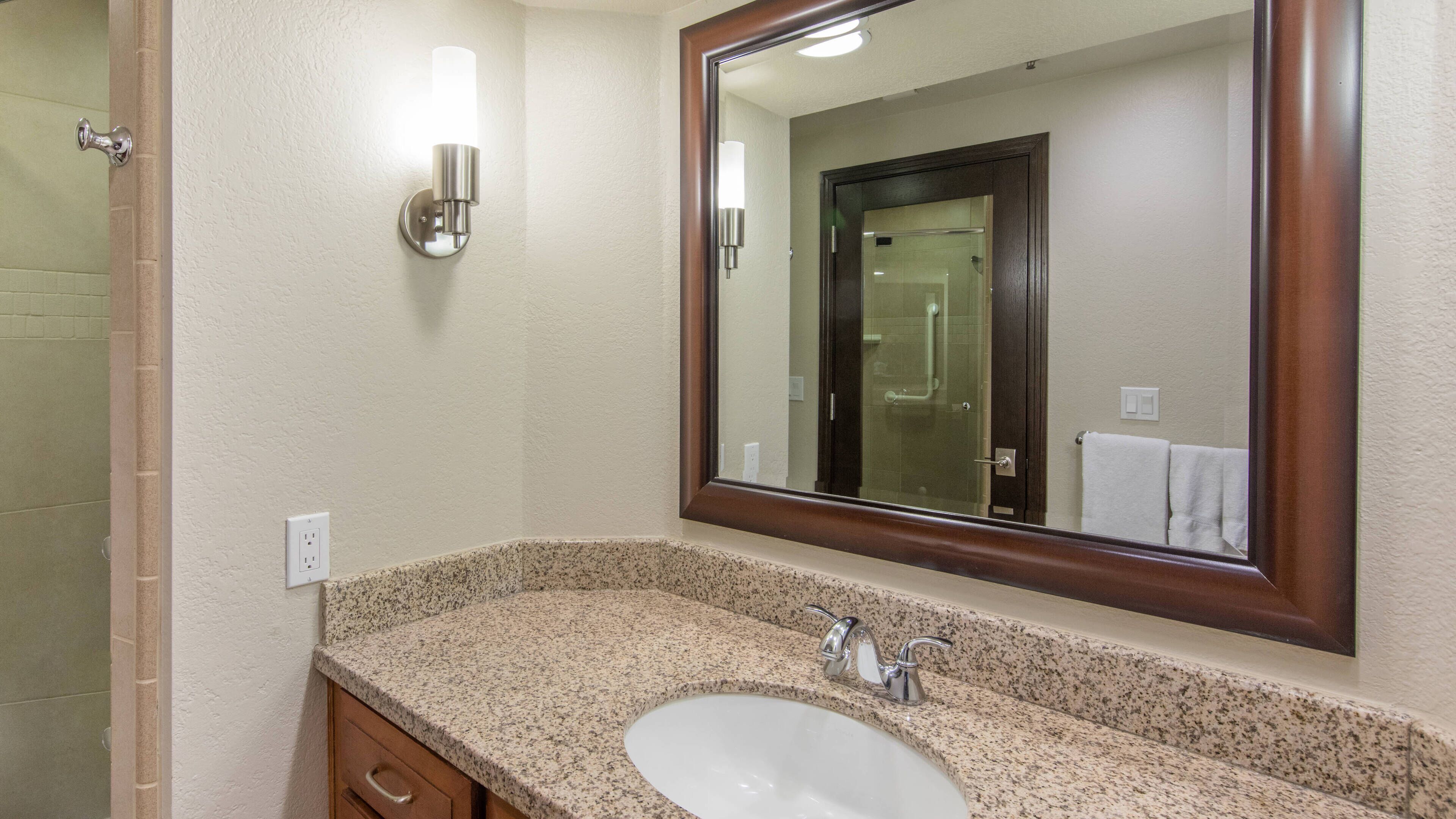 A bathroom with a granite countertop sink, a mirror, a towel rack, and a shower door.