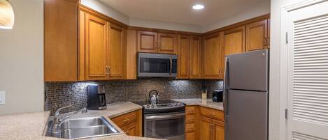 A kitchen with wooden cabinets, a stainless steel sink, a microwave, a stove, and a refrigerator.