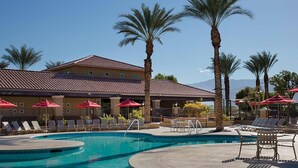 Ein Hotel mit Schwimmbad, Palmen und roten Sonnenschirmen.