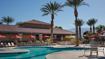 Un hotel con piscina, palmeras y sombrillas rojas.