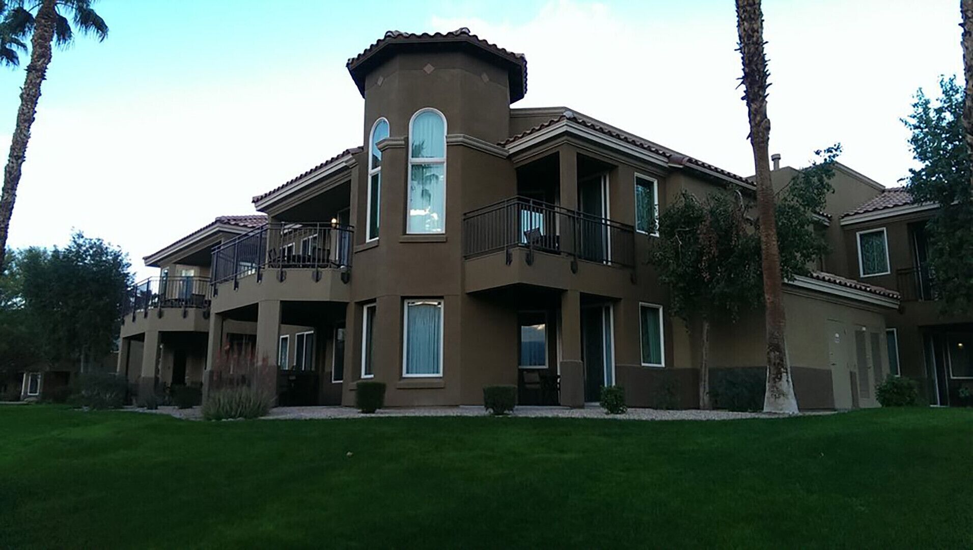 A multi-story residential building with balconies, large windows, and a well-maintained lawn.