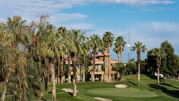 A golf course with a clubhouse, palm trees, and a clear sky.