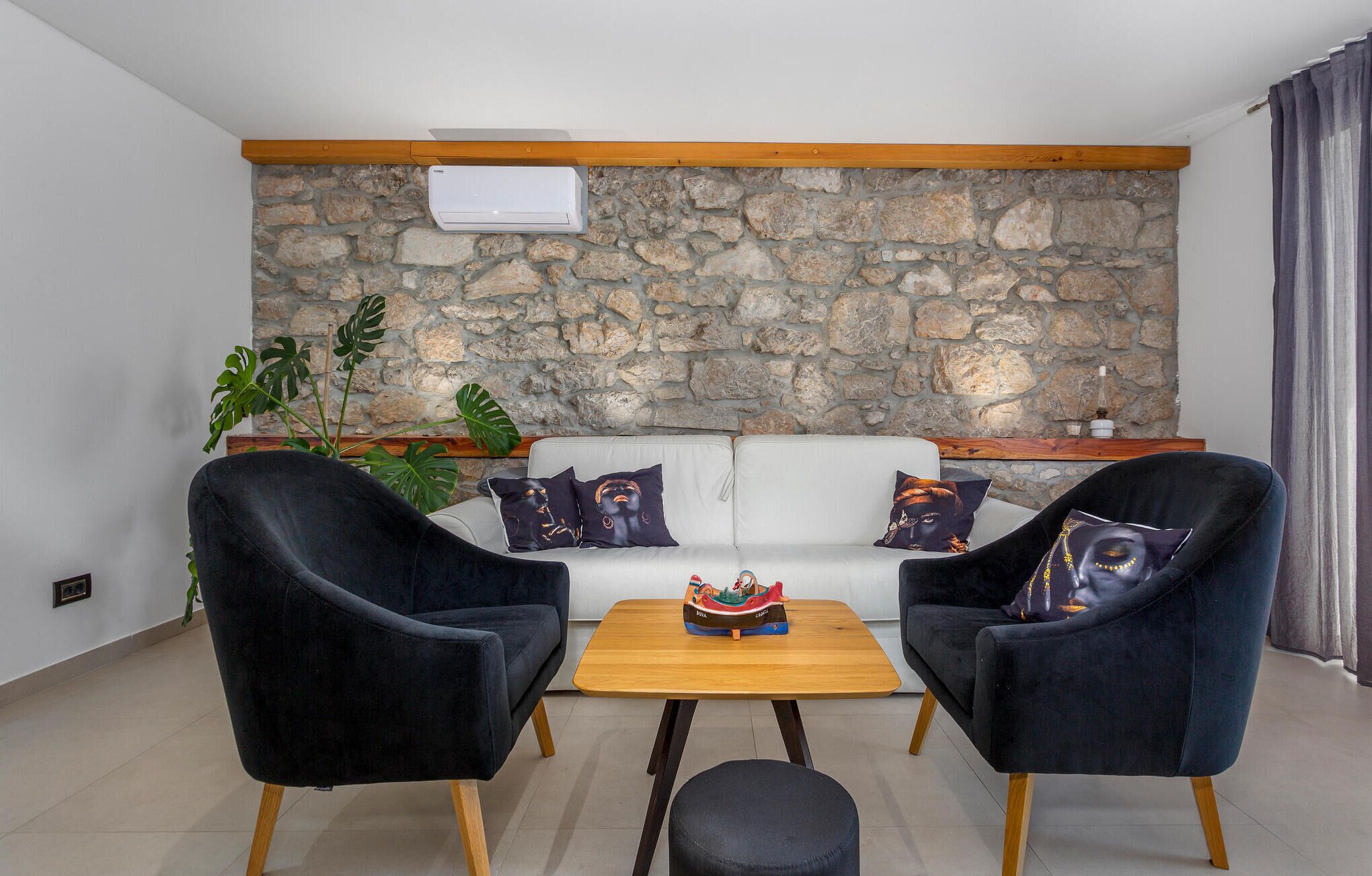 Een woonkamer met een stenen muur, een witte bank, twee zwarte fauteuils, een houten salontafel en een kamerplant.