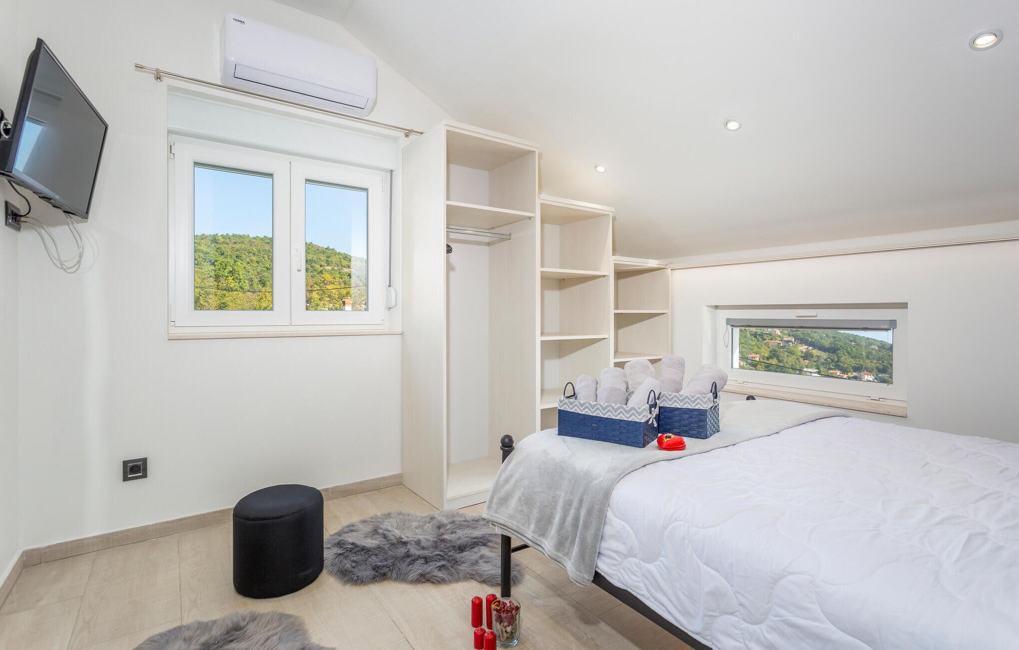 Une chambre à coucher comprenant un lit, une télévision, un climatiseur, une armoire et une fenêtre donnant sur un paysage verdoyant.