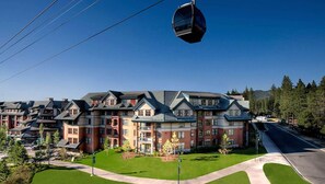 Ein mehrstöckiges Hotel mit moderner Architektur, das Ziegel- und Natursteinfassaden kombiniert und eine markante Seilbahn darüberführt.