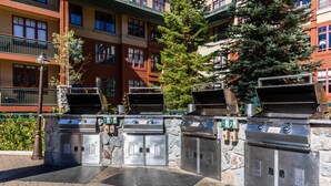 Un'area barbecue esterna con diverse postazioni, pareti in pietra e un edificio con balconi sullo sfondo.
