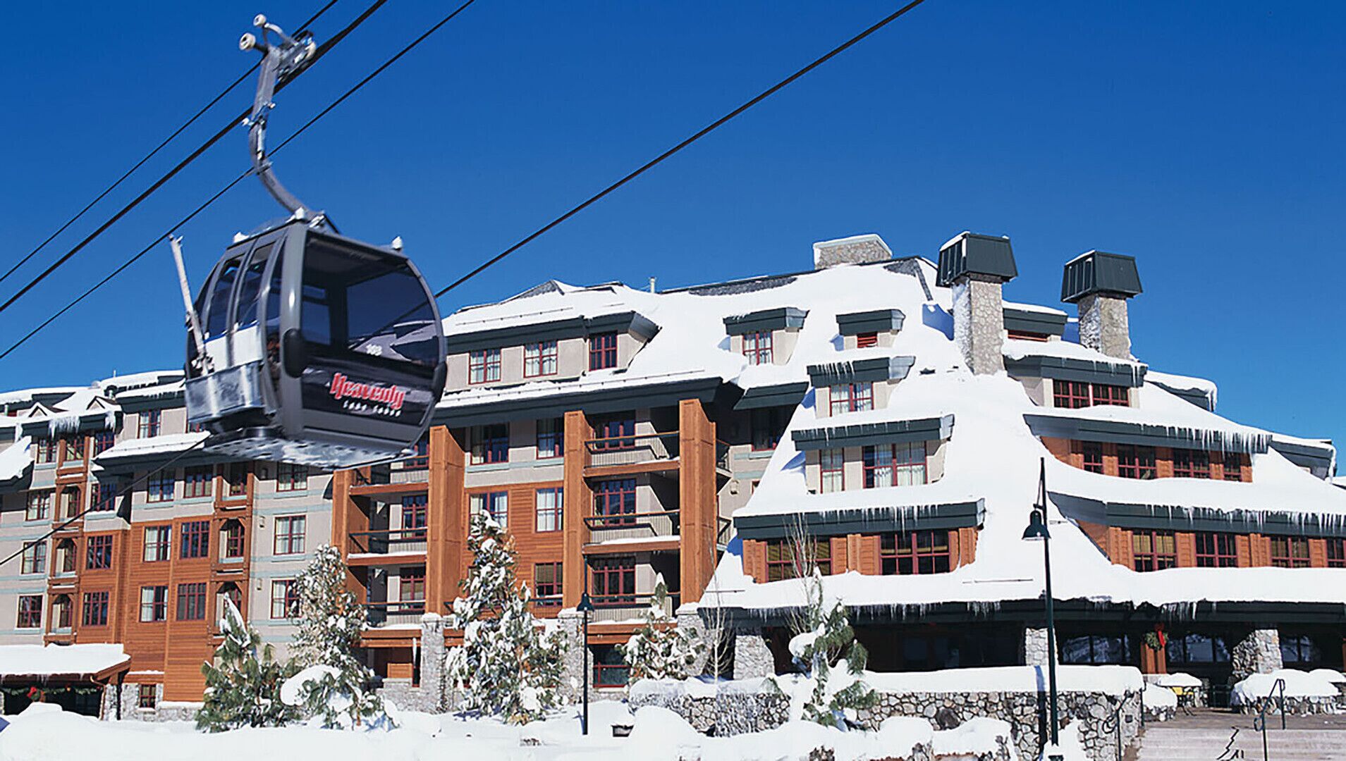 Un télésiège avec une pancarte, un immeuble à plusieurs étages doté de balcons et des arbres couverts de neige.