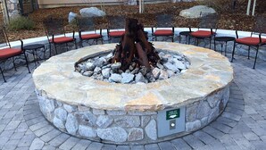Ein Steinkaminfeuerstelle umgeben von Stühlen mit roten Kissen, auf einer gepflasterten Terrasse.