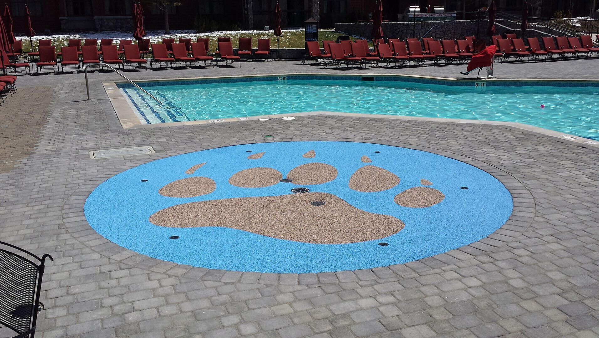A pool area with red lounge chairs and a blue paw print design on the ground.
