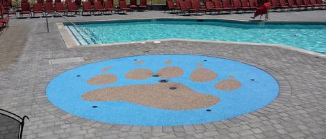 A pool area with red lounge chairs and a blue paw print design on the ground.