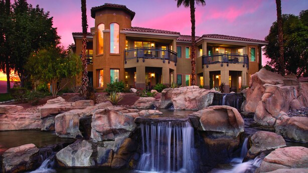 Un hotel con cascada, varios balcones y un jardín bien cuidado.