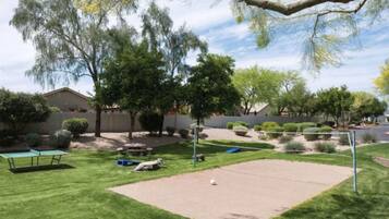 Un jardin avec une table de ping-pong, un petit espace de jeux et un filet de volley-ball.