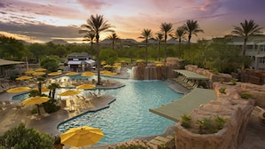 A resort pool area with multiple pools, sun loungers, and umbrellas.